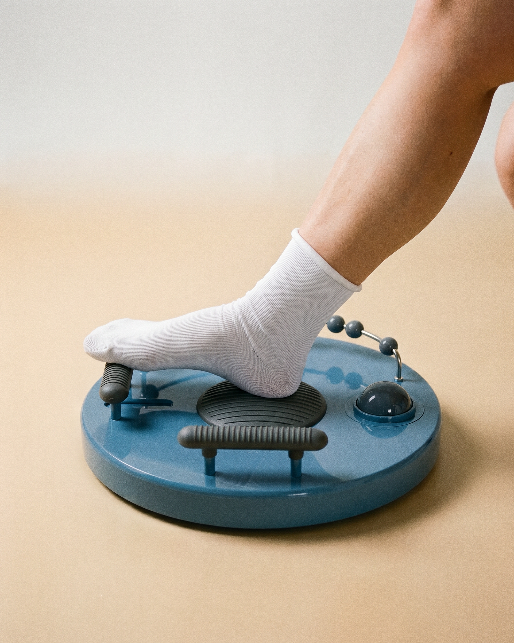 Person wearing a white sock on a blue foot massager against a beige background